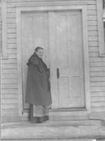 SA0033.5 - Sarah Collins was from the South Family. She is shown dressed in a hat and cape at the door of unidentified building., Winterthur Shaker Photograph and Post Card Collection 1851 to 1921c